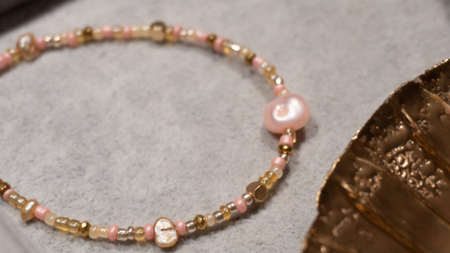 Armbånd med lyserøde og brune ferskvandsperler, glasperler i rosa, guld og orange og guldfarvede hæmatitperler. Håndlavet i vores smykkecafé, Smyk & Hyg i Vejle