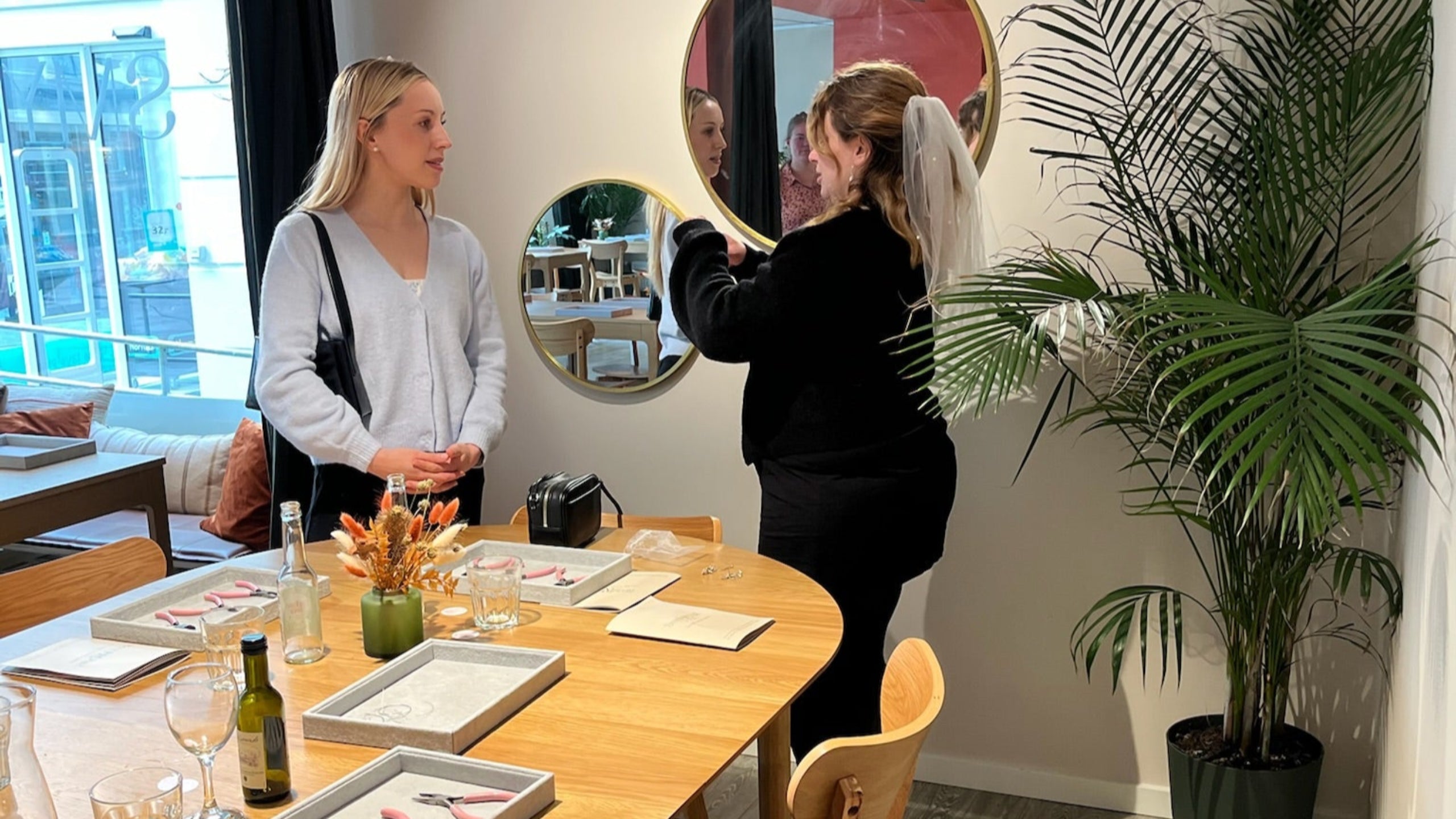 to veninder står foran spejlene i Smyk og Hygs lokale. Den ene af dem har et brudeslør på, da de fejrer hendes polterabend.