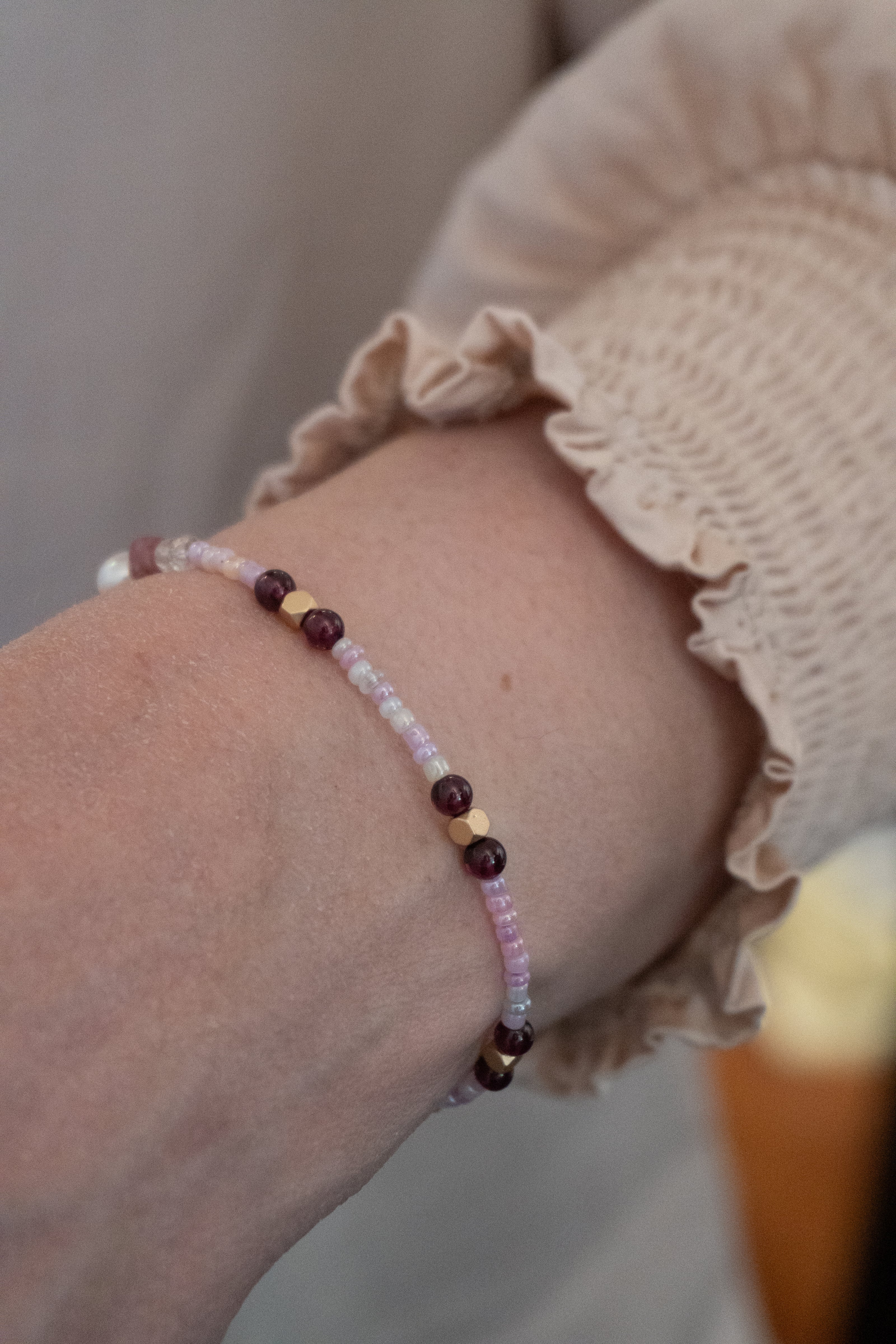 Armbånd med guldfarvede hæmatitperler, hvide og lyserøde glasperler og mørkerøde granatperler. Håndlavet i vores smykkecafé, Smyk & Hyg i Vejle