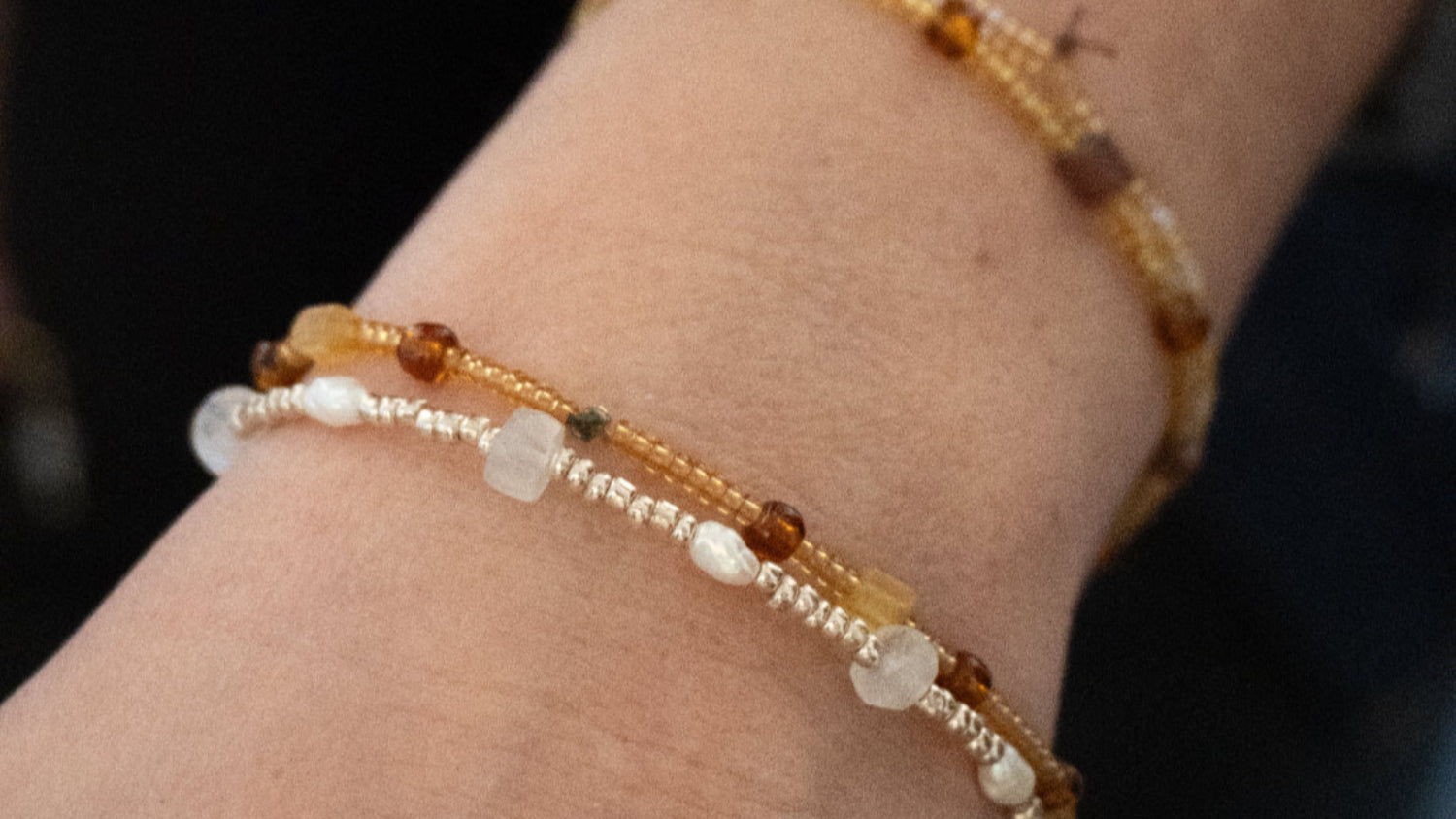 Armbåndssæt. Et med brune glasperler, ravperler, hæmatit perler, og carniolperler. Et andet med sølvfarvede glasperler, hvide ferskvandsperler og månestensperler. Håndlavet i vores smykkecafé, Smyk & Hyg i Vejle