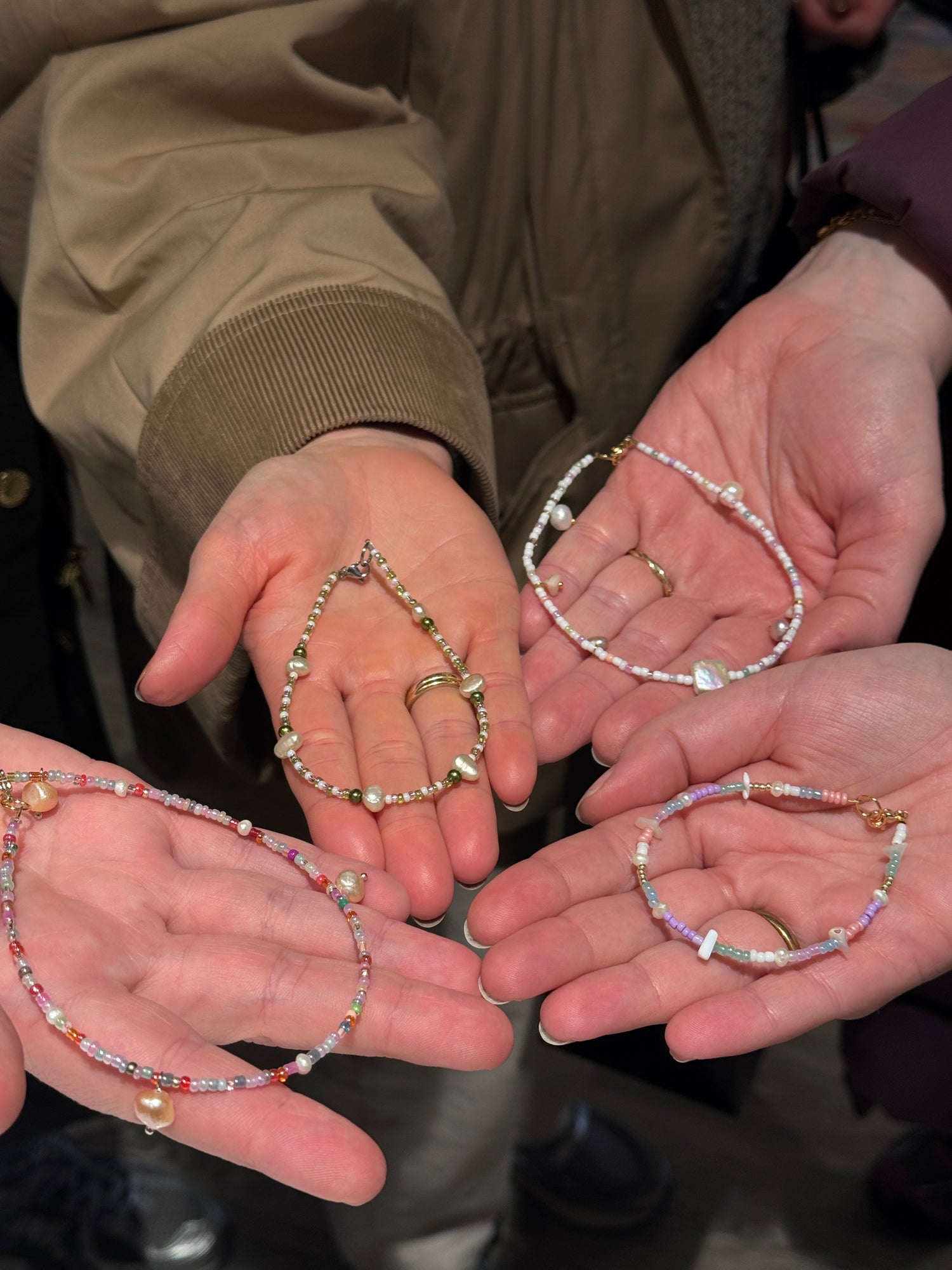 Hænder der holder håndlavede armbånd med perler og ferskvandsperler fra et hyggeligt babyshower hos Smyk&Hyg i Vejle