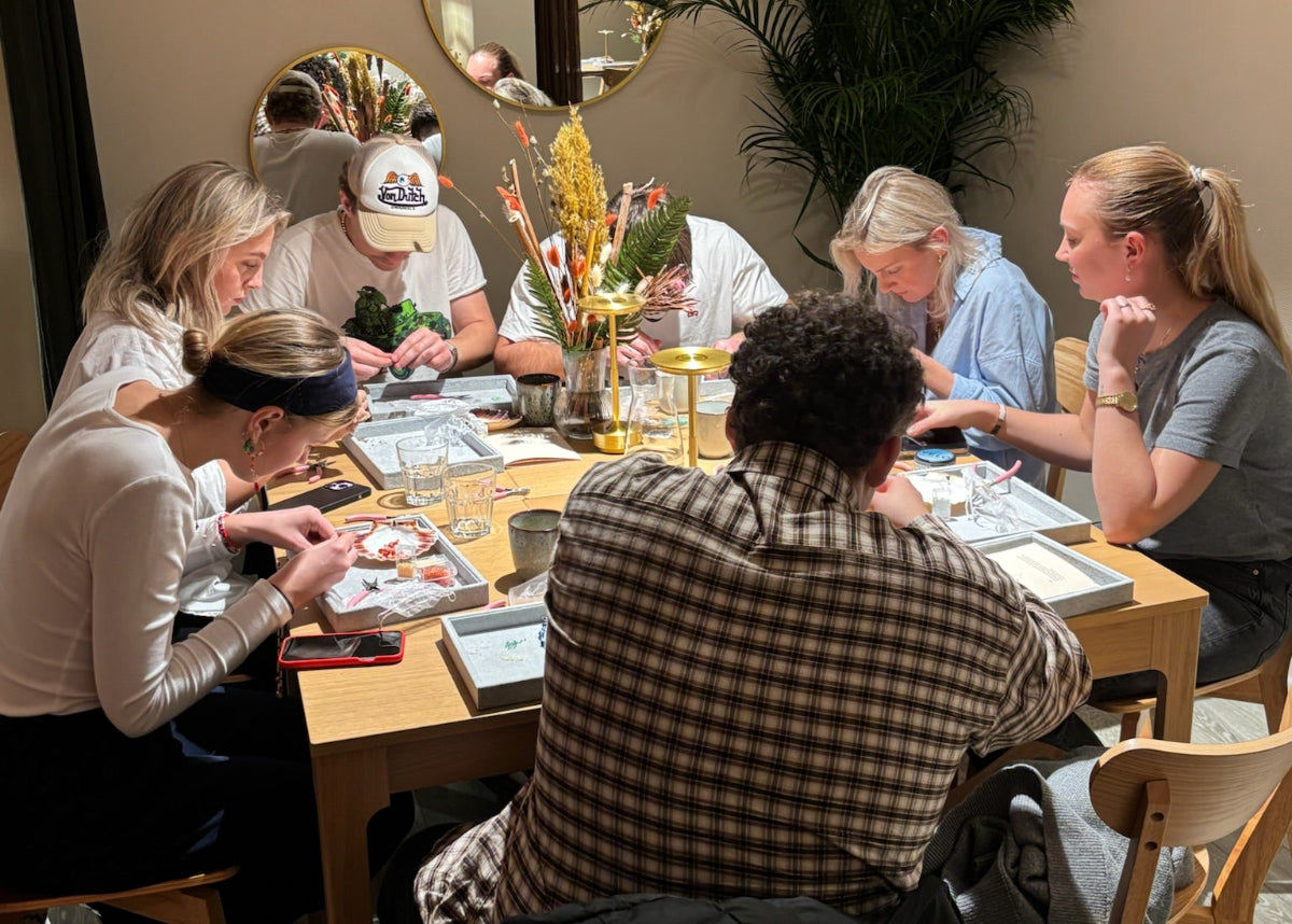 Gæster samlet til babyshower hos Smyk&Hyg i Vejle, hvor de laver personlige smykker sammen omkring et bord i en hyggelig og kreativ smykkecafé.