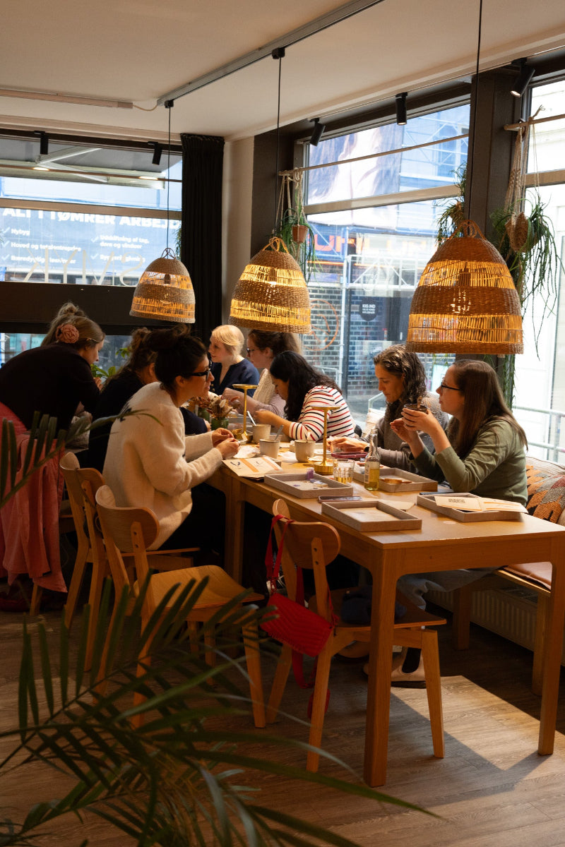 Kvinder samlet til babyshower hos Smyk&Hyg i Vejle, hvor de hygger sig med at lave smykker ved et bord i en varm og afslappet atmosfære