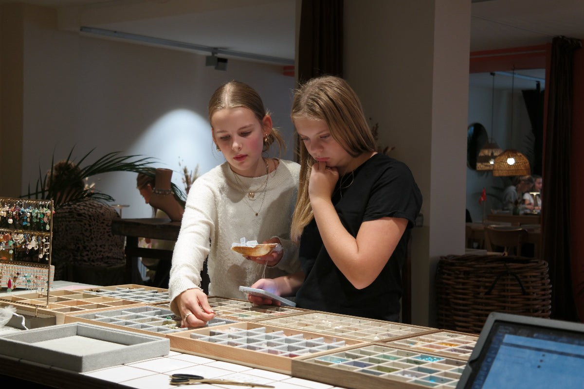 To piger stå og beslutter hvilke perler de skal vælge fra smykkecaféens perleudvalg.