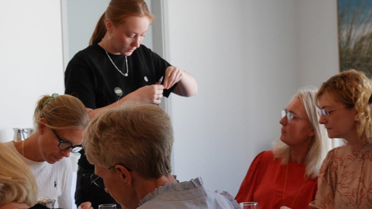 Deltagere til firmaarrangement sidder samlet om bord og laver smykker under en kreativ workshop ud af huset med Smyk&Hyg – en hyggelig teambuilding aktivitet for virksomheder.