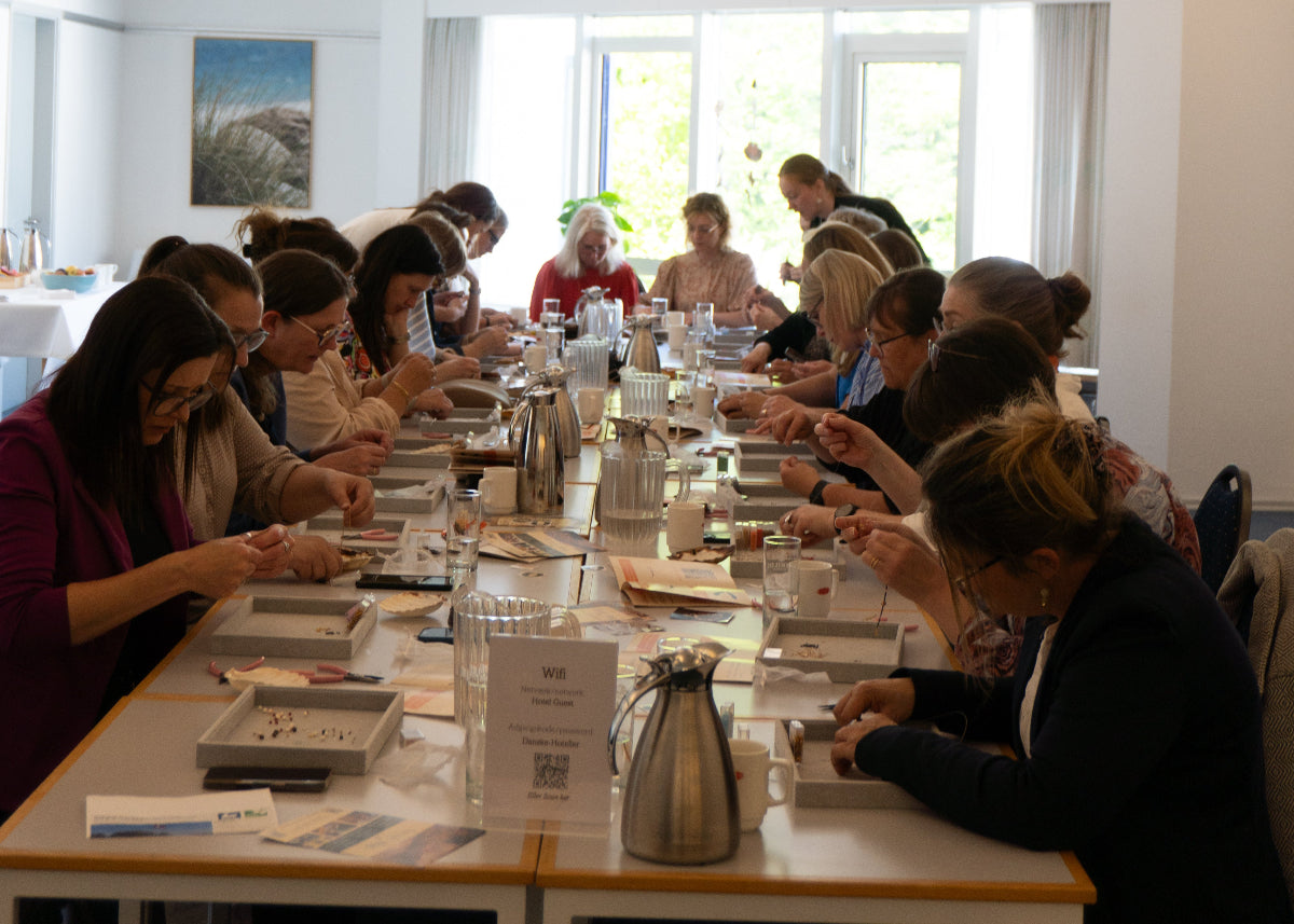 Større gruppe medarbejdere deltager i firmaarrangement og laver smykker sammen ved langborde under en kreativ teambuilding workshop ud af huset med Smyk&Hyg i Vejle.
