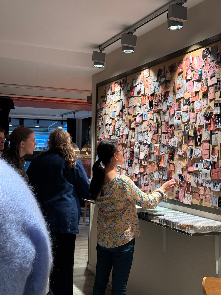 Deltagere til firmaarrangement hos Smyk&Hyg i Vejle står samlet og vælger smykkedesign ved inspirationsvæg under kreativ workshop og teambuilding