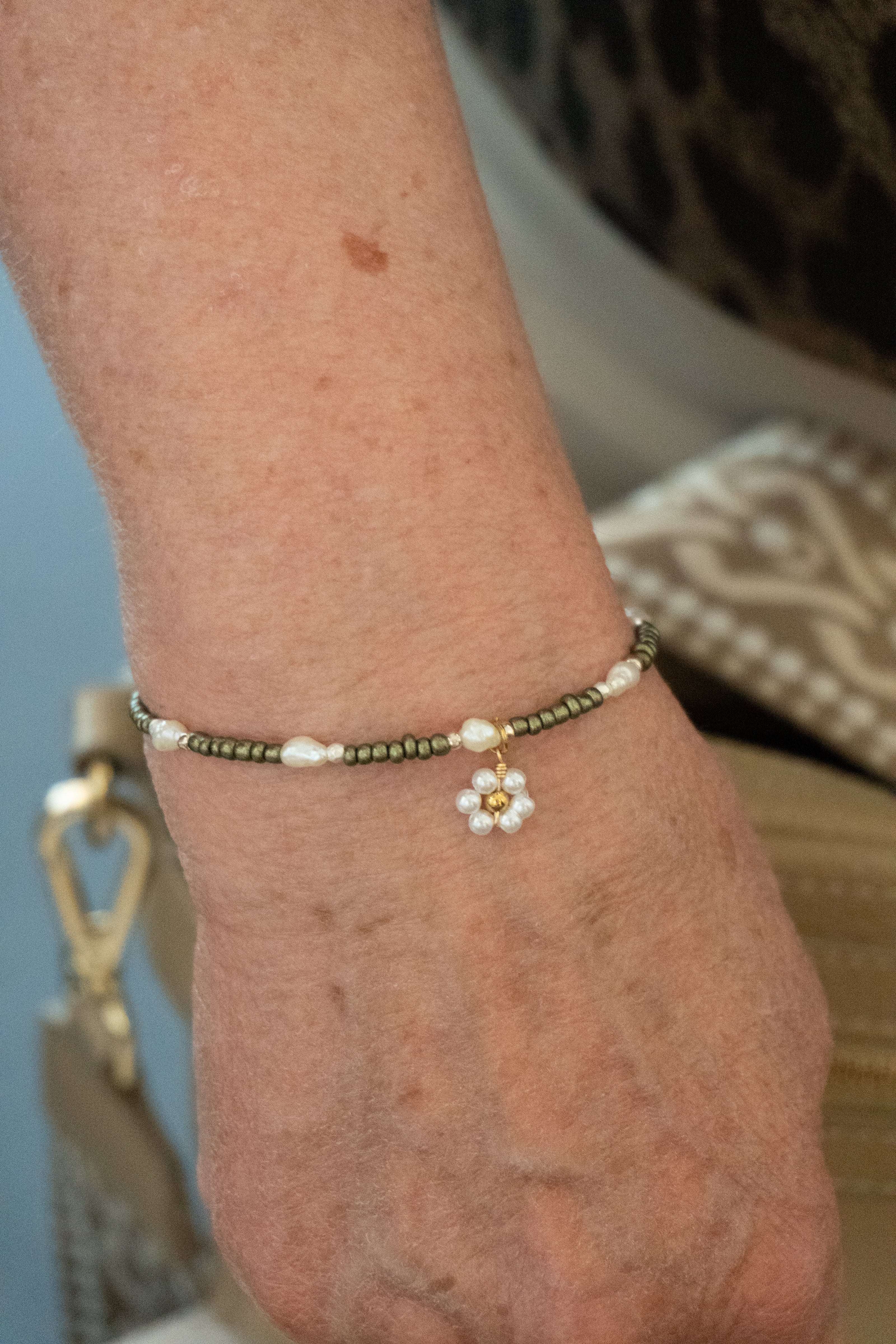 Armbånd designet af kunde med perler i grøn og guld, hvide ferskvandsperler og et blomstervedhæng. Håndlavet i vores smykkecafé, Smyk & Hyg i Vejle
