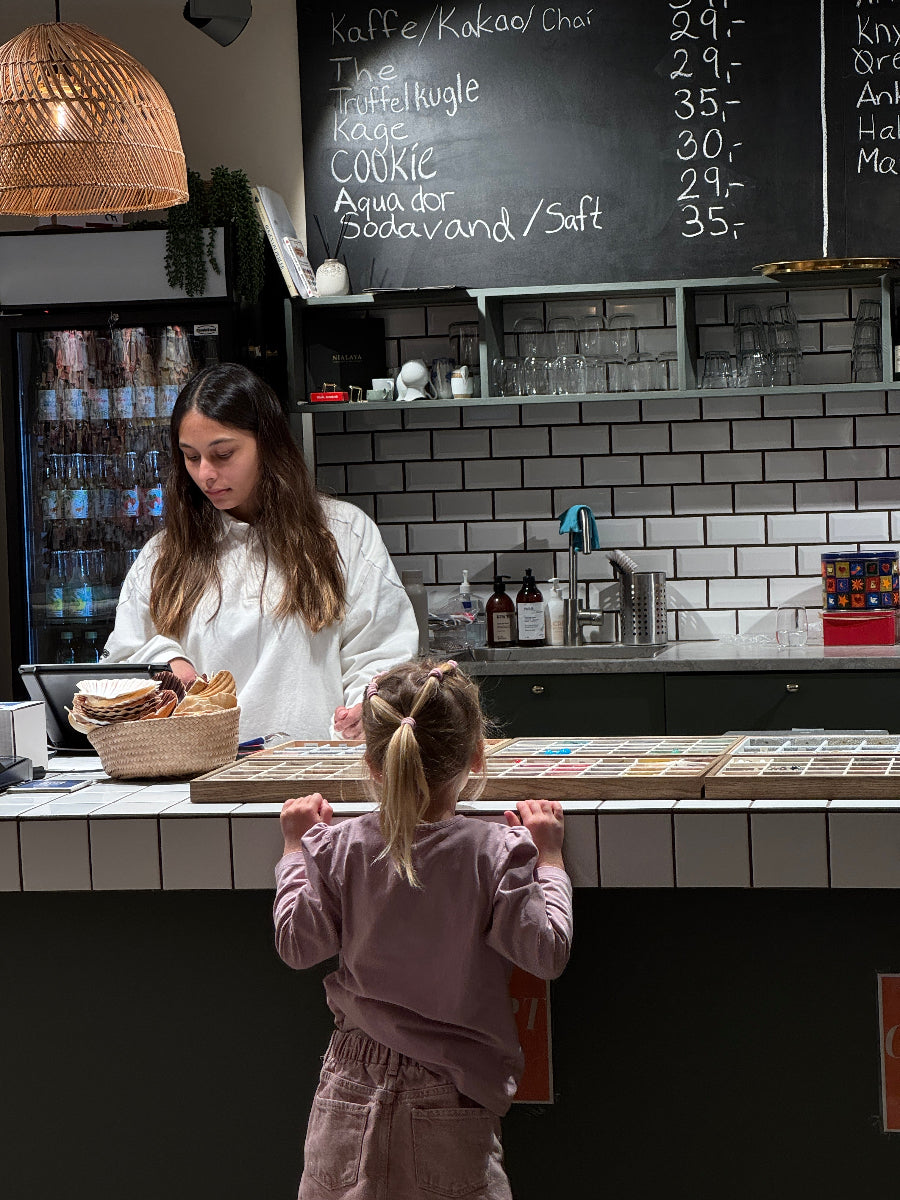 Barn står ved disken i en hyggelig smykkecafé og vælger perler til smykkelavning ved børnefødselsdag hos Smyk&Hyg i Vejle