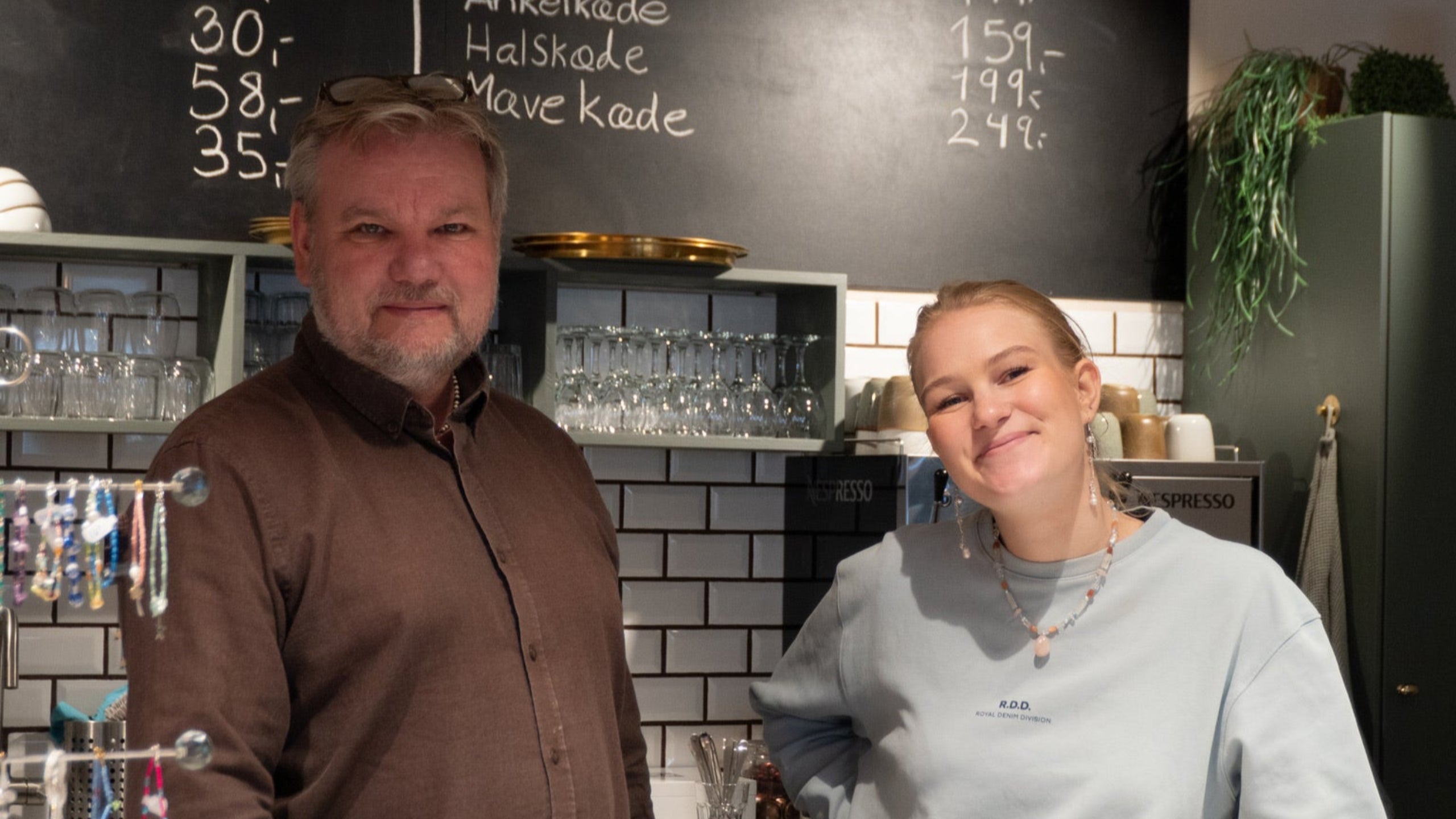 To ansatte fra Smyk og Hyg står og smiler imødekommende bag disken i smykkecaféen. 