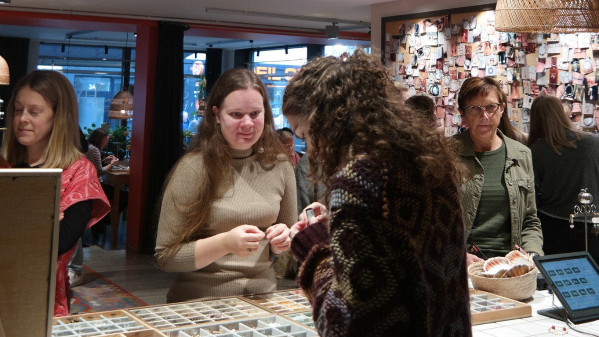 Gæster samles omkring perler og materialer under fødselsdagsfejring hos Smyk&Hyg i Vejle, hvor man kan holde kreativ fødselsdag og lave sine egne smykker i hyggelige omgivelser.
