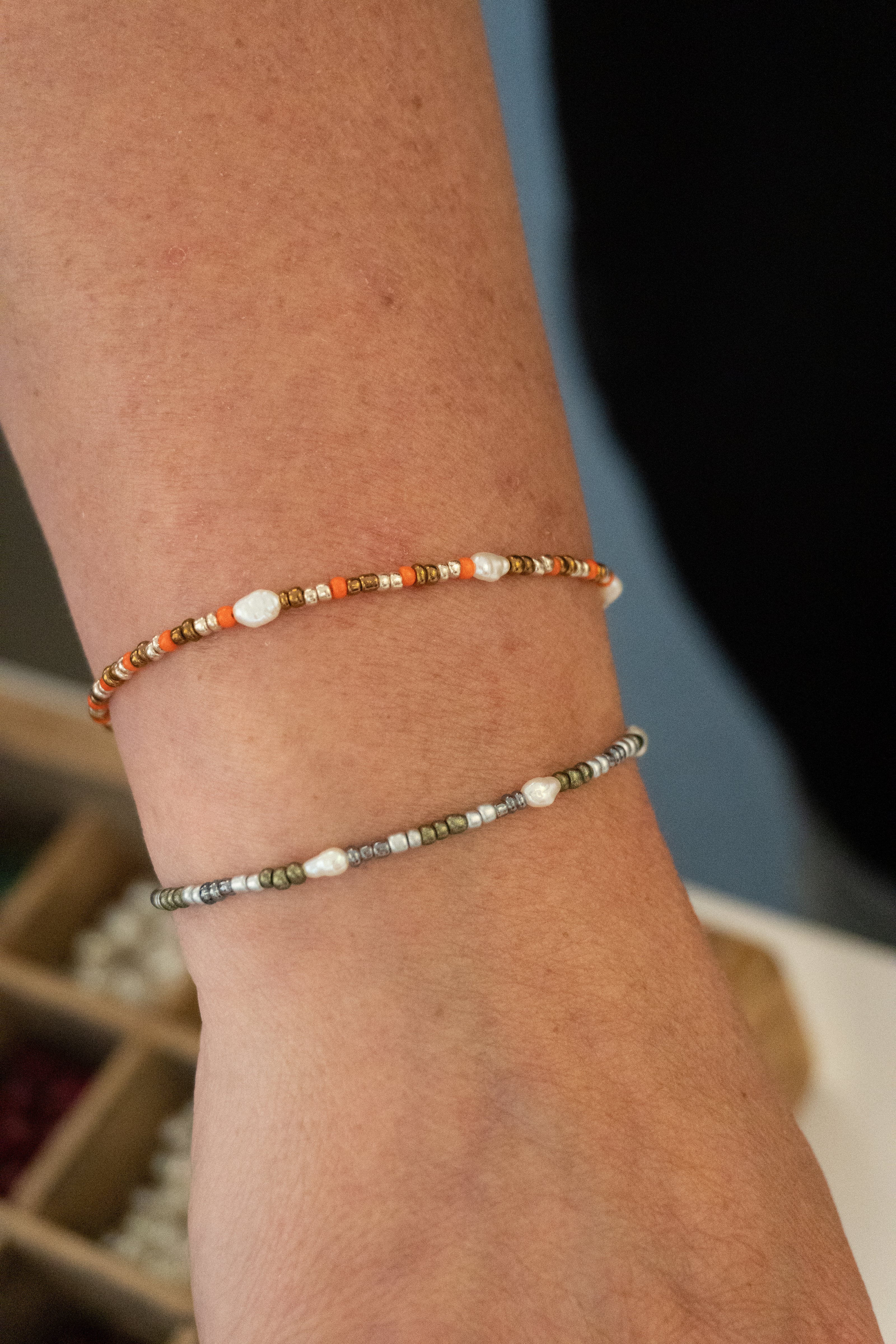 To armbånd designet af en kunde. Et med orange, hvide og brune glasperler og hvide ferskvandsperler. Et andet med grønne, hvide og grå glasperler og hvide ferskvandsperler. Håndlavet i vores smykkecafé, Smyk & Hyg i Vejle