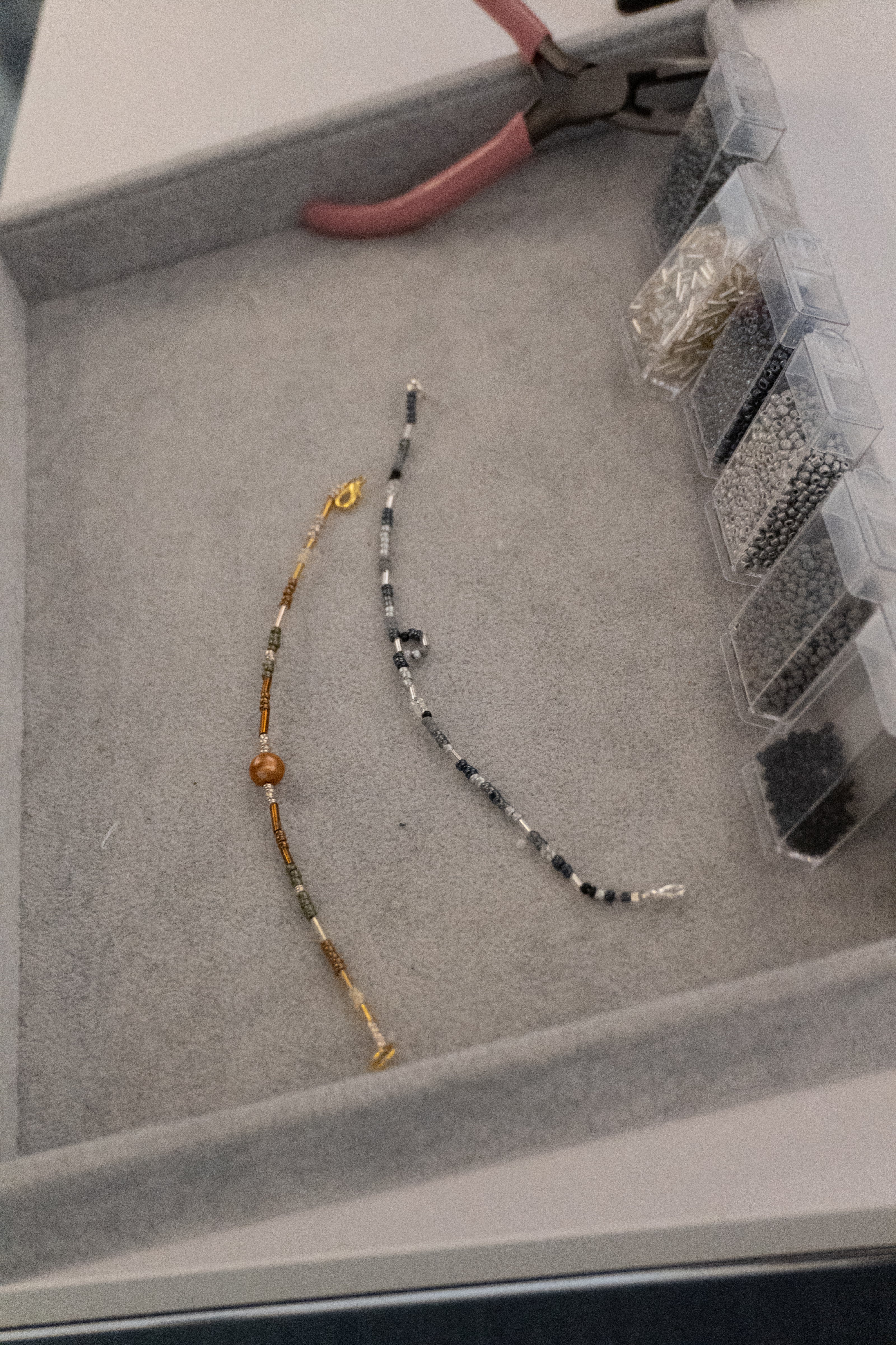 Armbåndssæt. Et i guld med brune, grå guldfarvede, sølvfarvede og gennemsigtige glasperler samt en brun ferskvandsperle i midten. Et andet i sølv med sølvfarvede, sorte og grå glasperler. Håndlavet i vores smykkecafé, Smyk & Hyg i Vejle