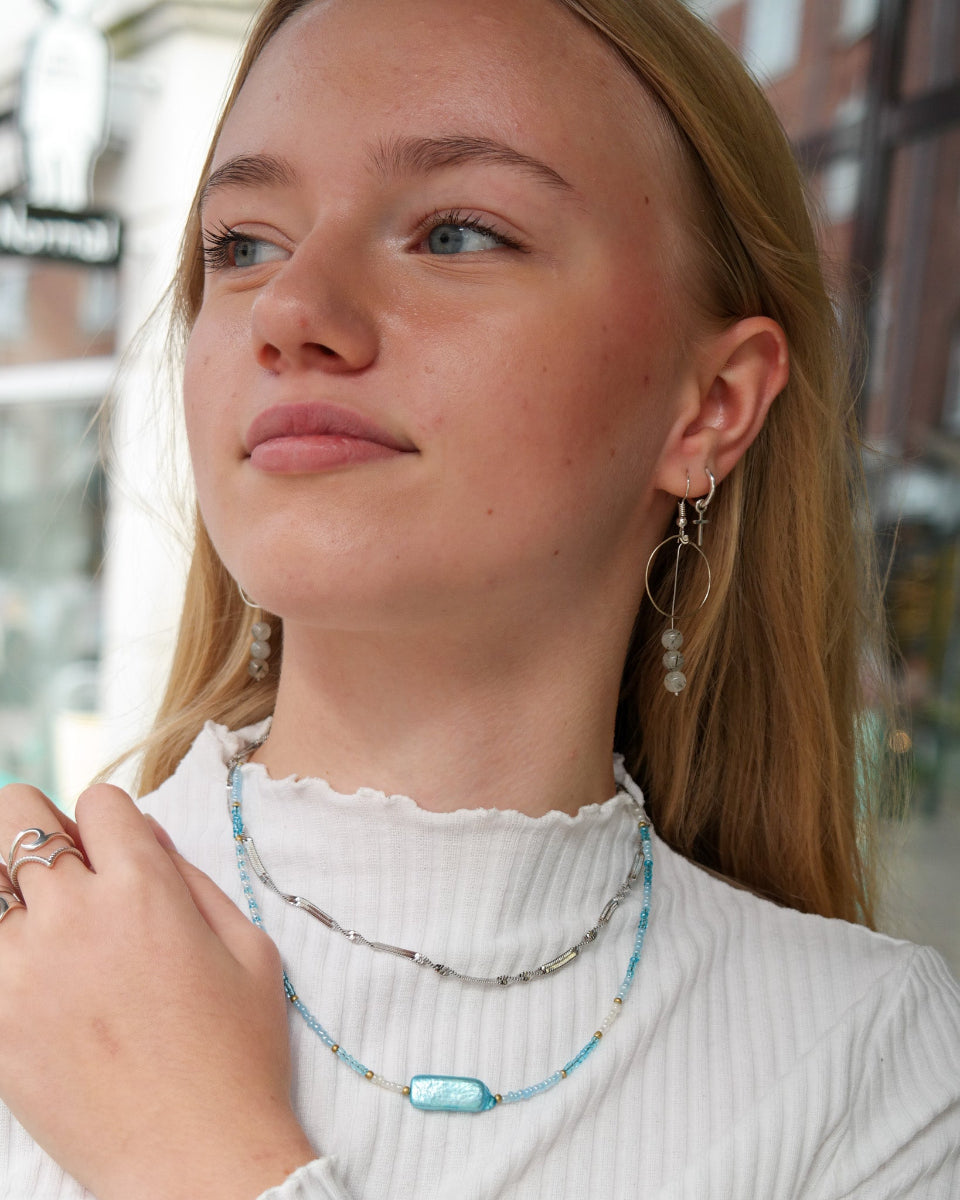Model med mix af vandfaste smykker og håndlavede smykker fra Smyk&Hyg – lag-på-lag styling med halskæder og øreringe i Vejle
