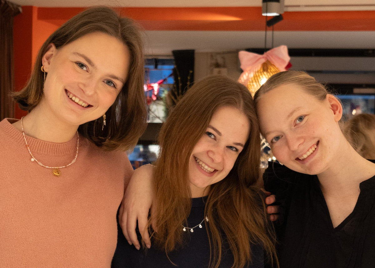 Tre smilende kvinder står tæt sammen i Smyk&Hyg i Vejle og viser deres smykker frem i en varm og hyggelig atmosfære.