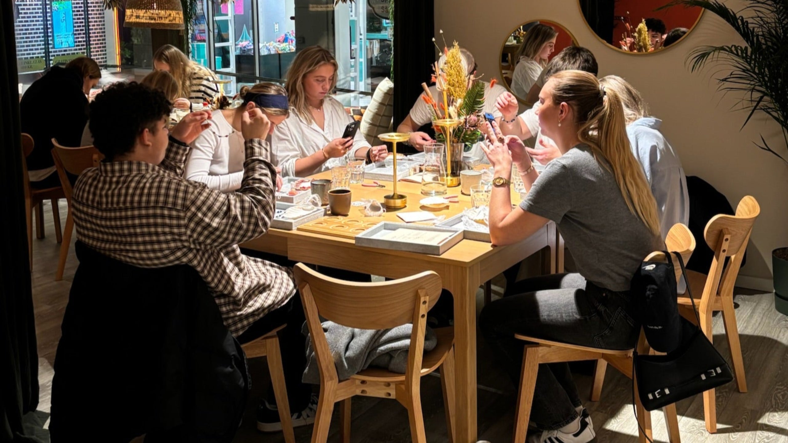 En gruppe sidder om et rundbord og er igang med at lave smykker i forbindelse med en fødselsdag hos Smyk og Hyg.